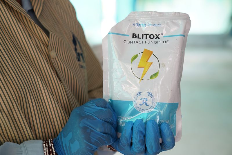 Two hands in blue gloves hold up a white and blue foil packet printed with a lightning-bolt graphic, against a striped shirt.