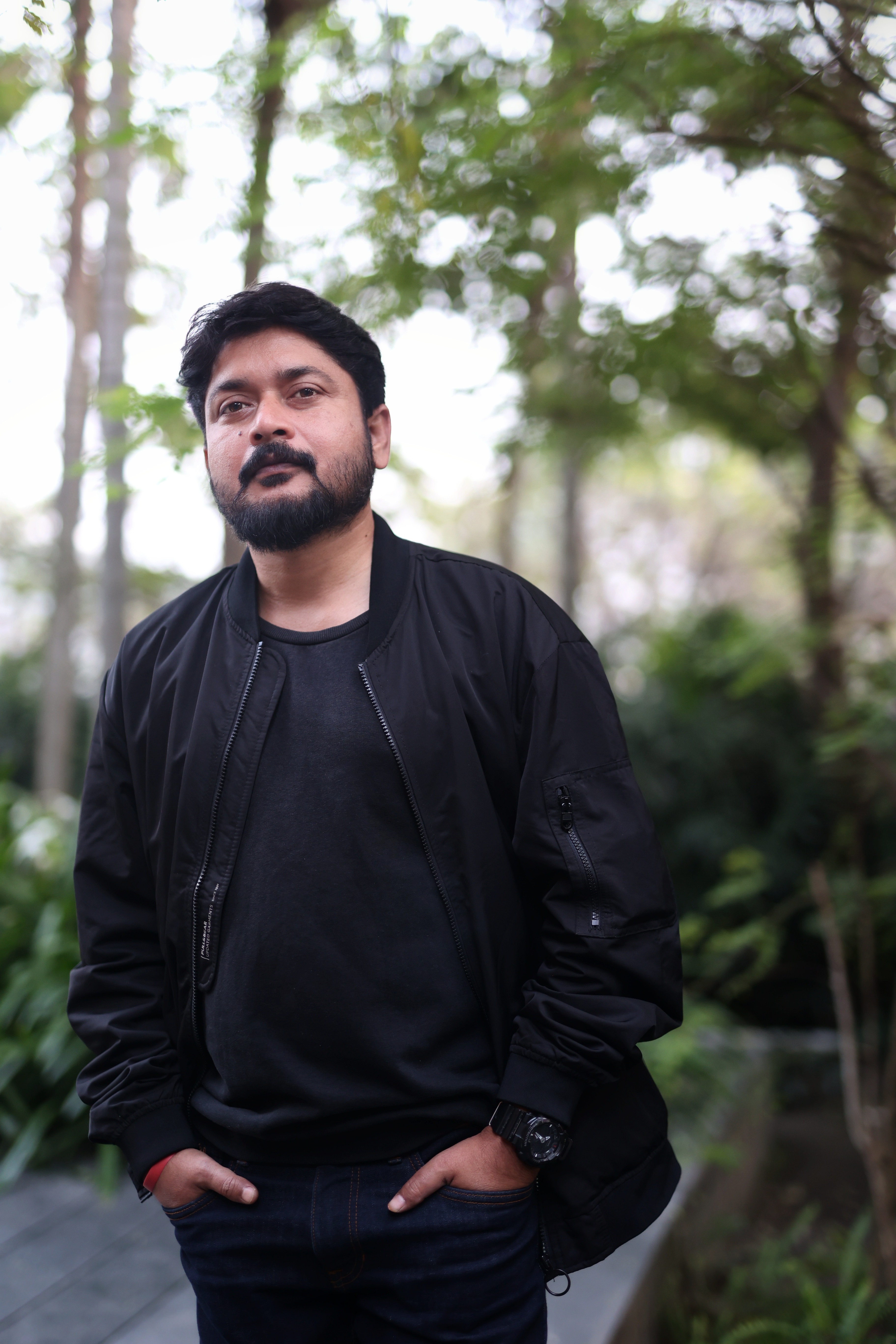 Nilanjan Karmakar standing outdoors in a black jacket beneath trees, looking towards the camera